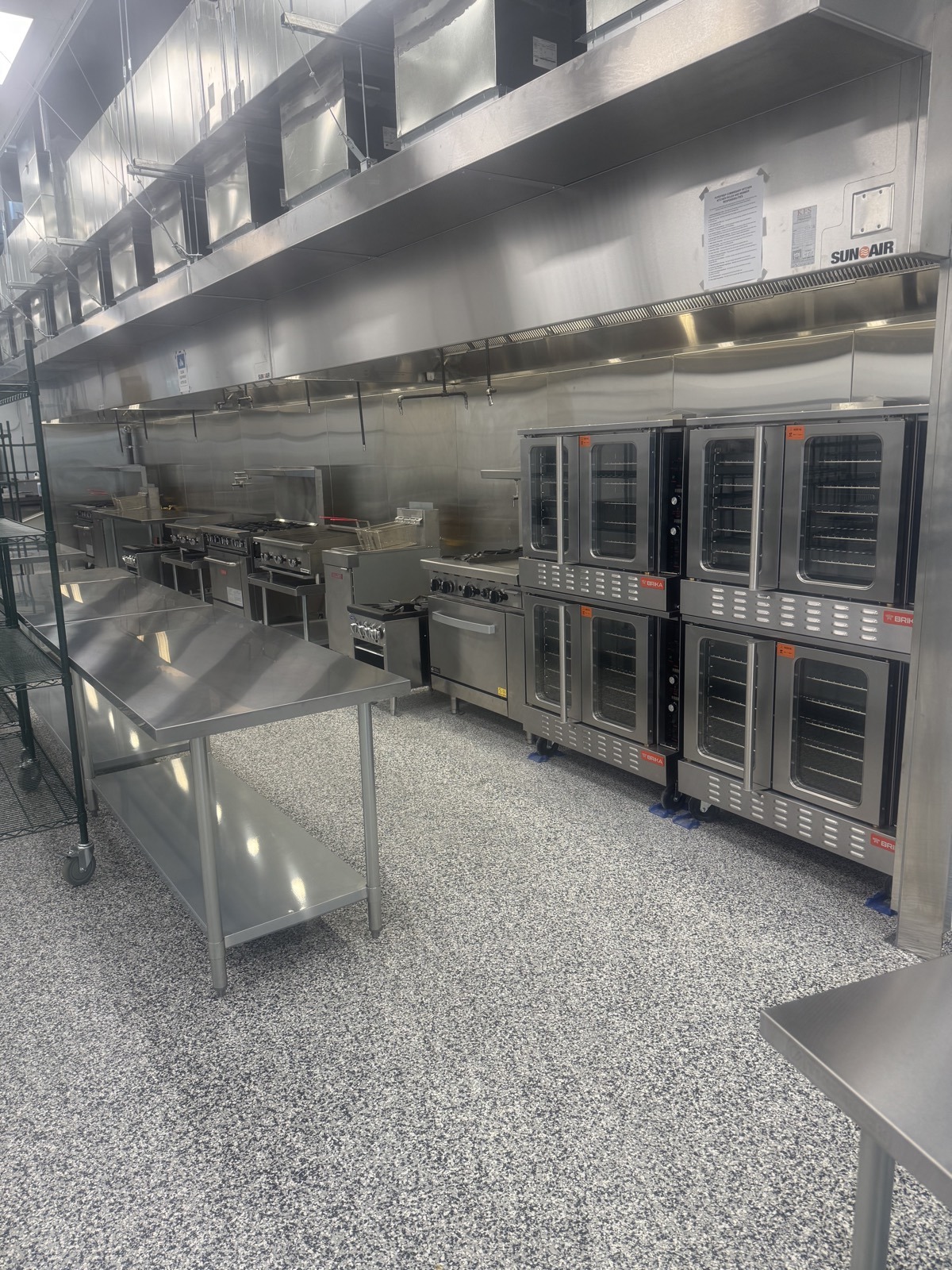 Commercial cookline and stacked ovens under ventilation hoods