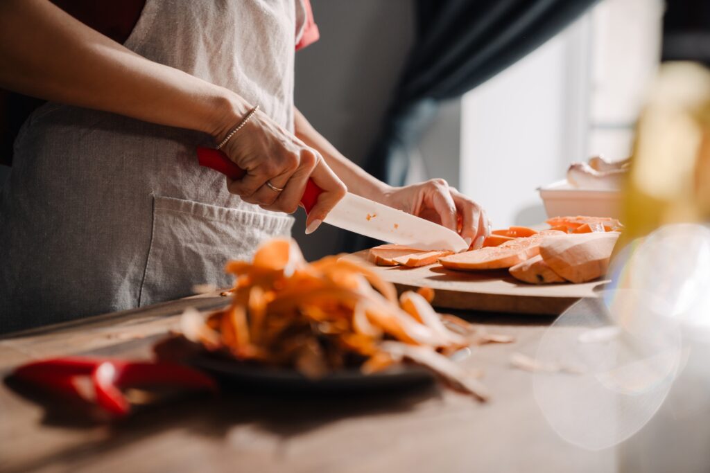 Young woman cutting sweet potato while cooking in kitchen